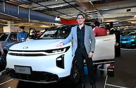 Hombre en traje claro junto a automóvil modelo S7, posando en evento de movilidad con fondo de otras personas y autos.
