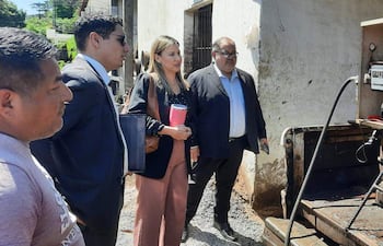 Cuatro personas conversan frente a una estructura clara; una mujer sostiene un vaso y dos hombres observan, en un ambiente de evaluación.