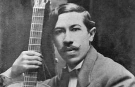 Agustín Barrios Mangoré luce traje claro con flor en la solapa, sosteniendo una guitarra en un fondo oscuro.