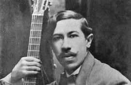 Agustín Barrios Mangoré luce traje claro con flor en la solapa, sosteniendo una guitarra en un fondo oscuro.
