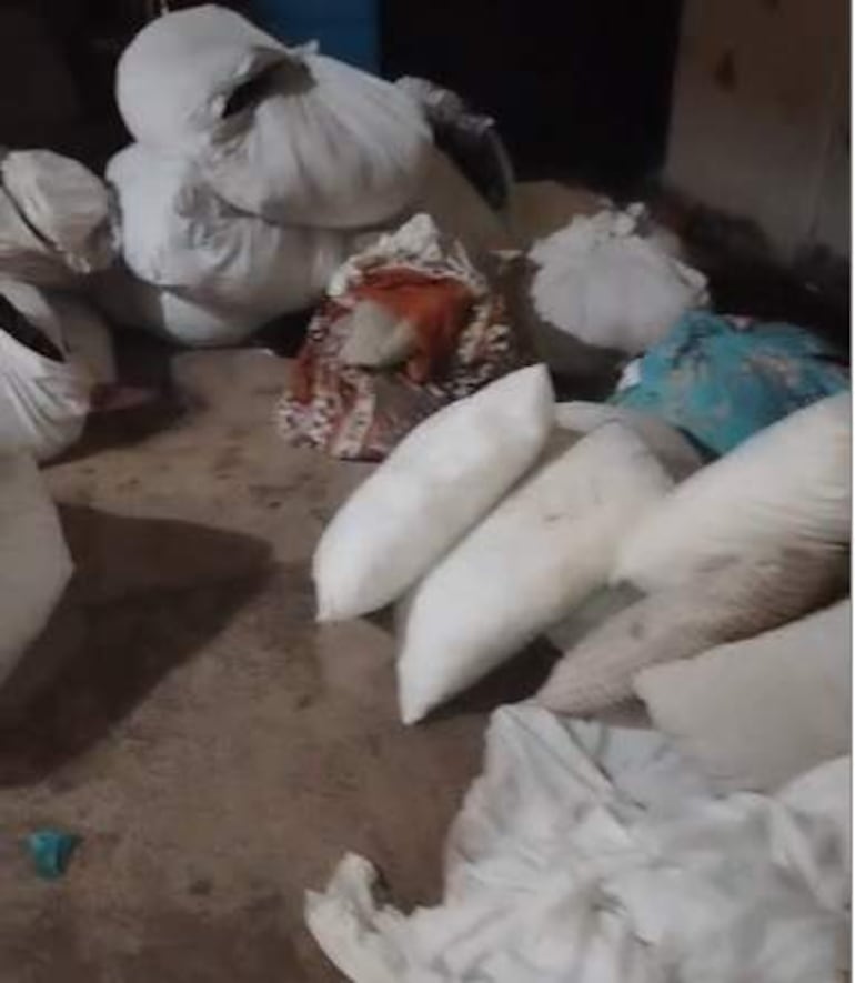 Ambiente desordenado y oscuro con bultos de ropa esparcidos por el suelo en la lavandería del hospital.