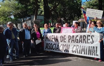 Un grupo de aproximadamente 15 personas se manifiestan al aire libre con carteles contra la mafia de los pagarés, en un día soleado.