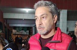 Mario Abdo Benitez con chaleco rojo y camiseta oscura, rodeado de reporteros con micrófonos, en un ambiente de entrevista.