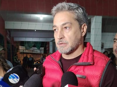 Mario Abdo Benitez con chaleco rojo y camiseta oscura, rodeado de reporteros con micrófonos, en un ambiente de entrevista.