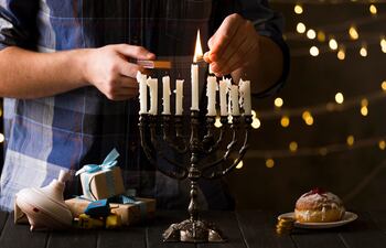 Un hombre enciende una de las velas blancas de una menorá (también conocida como januquía o candelabro de Hanukkah) en un ambiente cálido y festivo.