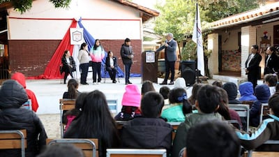 Roberto Schael habla a niños en un acto formal, algunos llevan ropa de abrigo y el ambiente tiene banderas decorativas.