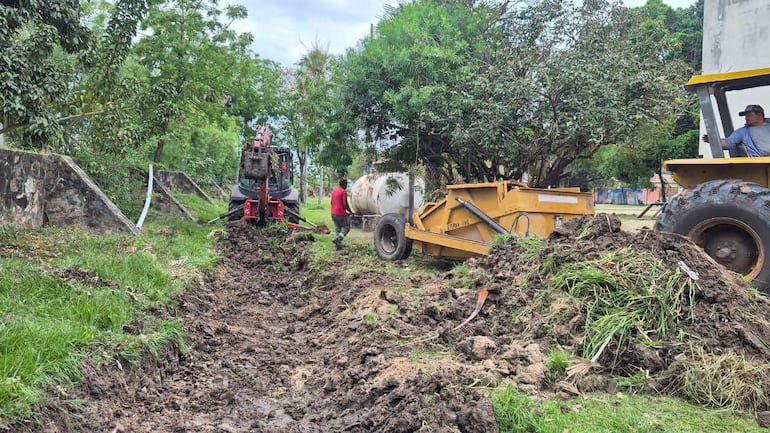 Tres hombres trabajan en un campo; uno viste camiseta roja, otro opera un tractor y el tercero está en la cabina.