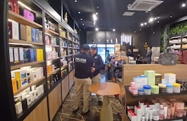 Tres agentes de policía conversan en una tienda de productos de belleza, con estanterías cargadas de cosméticos en el fondo.