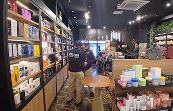 Tres agentes de policía conversan en una tienda de productos de belleza, con estanterías cargadas de cosméticos en el fondo.
