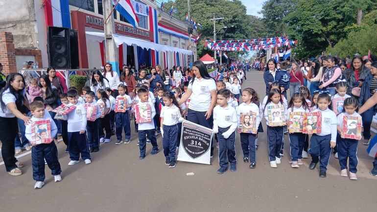 Niños de la escuela educativa 314 básica N°1 desfilan con camisetas blancas, guiados por una docente en un ambiente festivo.