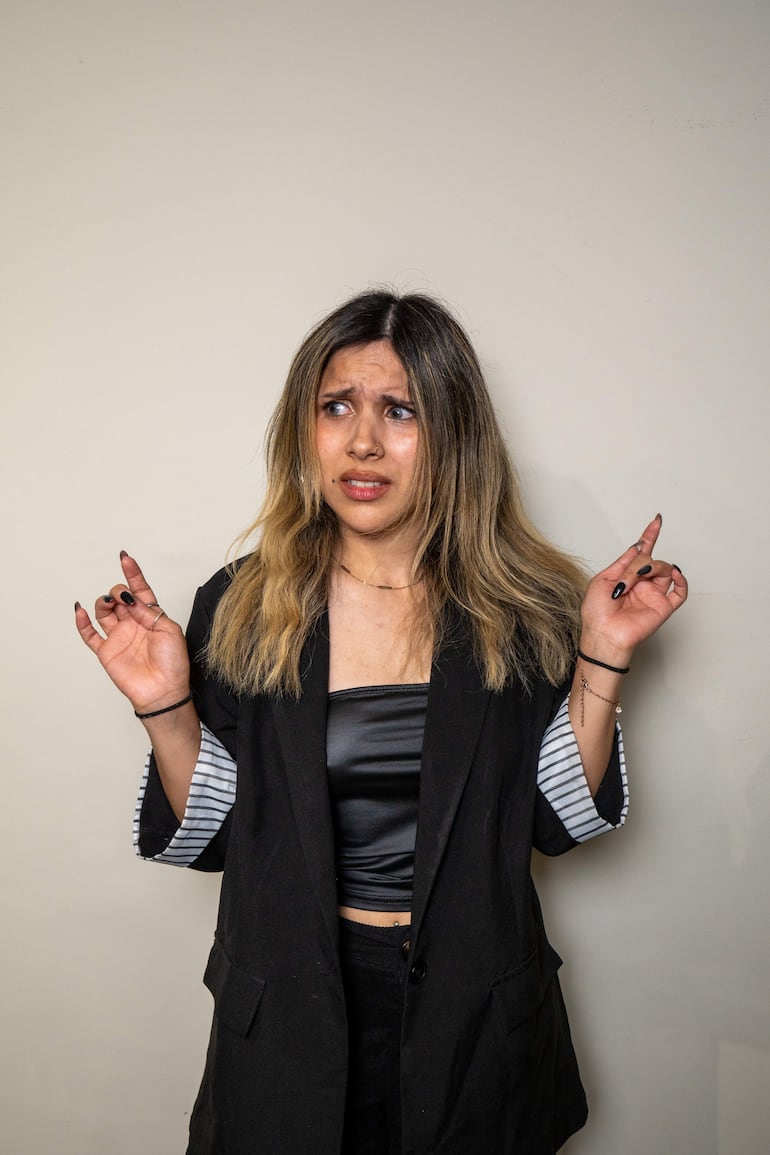 Mujer con cabello rubio oscuro y blazer negro, mostrando expresión de sorpresa con manos levantadas en un ambiente claro.