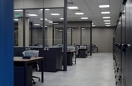 Oficina moderna y minimalista del MEC, con escritorios y sillas cubiertos de plástico, sin presencia de personas.