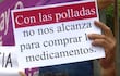 Persona sostiene un cartel que dice 'Con las polladas no nos alcanza para comprar los medicamentos', rodeada de otras personas en un ambiente urbano.