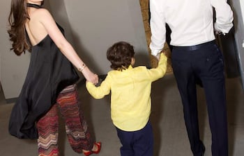 Nadia Ferreira con blusa negra y pantalones zigzagueantes, sostiene de la mano a un niño con camisa amarilla en un pasillo.