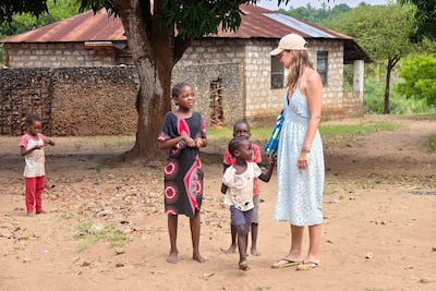 África Oriental: una turista blanca y niños africanos pobres socializan en una aldea keniata. Trabajo voluntario benéfico en países del tercer mundo.