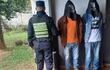 Policía con uniforme observa a dos hombres encapuchados, uno con camiseta naranja y otro blanca, en un entorno verde.