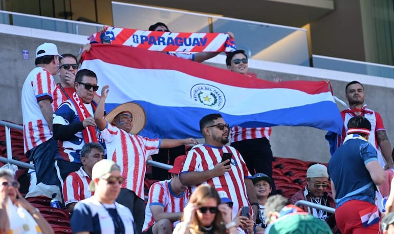 Grupo de hinchas paraguayos en el estadio, vestidos con camisetas rojas y blancas, un niño con sombrero gesticulando con alegría.