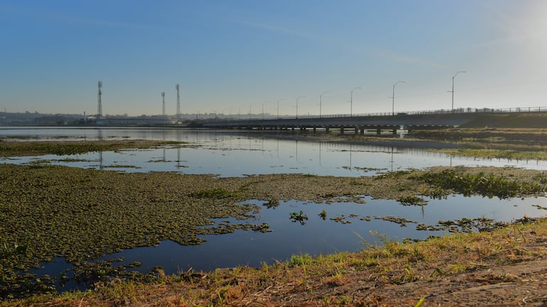Un tranquilo paisaje acuático con un puente visible y torres al fondo, sin personas en la escena.