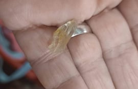 Fragmento de vidrio amarillo y translúcido sostenido con una mano, fondo difuso sin personas visibles.