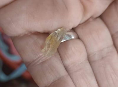 Fragmento de vidrio amarillo y translúcido sostenido con una mano, fondo difuso sin personas visibles.