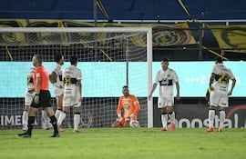Richard Sánchez y otros jugadores de fútbol en camisetas blanco y negro, lucen desanimados en el campo tras una jugada.