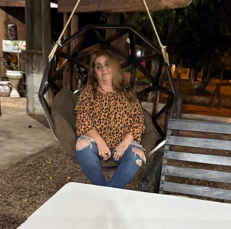 Mujer con blusa de leopardo y jeans sentada en silla colgante, en un ambiente acogedor con decoración de fondo.