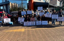 Grupo de adultos sosteniendo carteles sobre inclusión para niños con TEA y síndrome de Down en un ambiente exterior soleado.