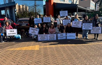 Grupo de adultos sosteniendo carteles sobre inclusión para niños con TEA y síndrome de Down en un ambiente exterior soleado.
