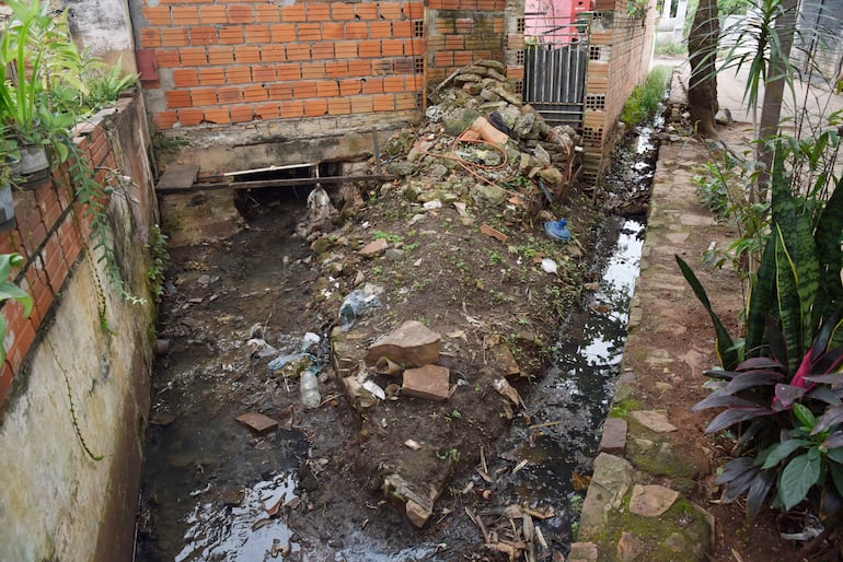Canal de desagüe sucio y estancado rodeado de residuos en un área residencial de Bo San Pablo.