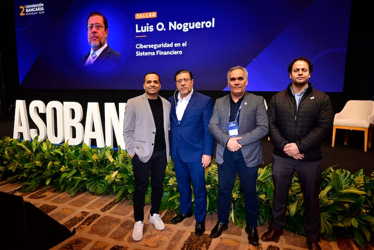 Cuatro hombres sonriendo en traje, ante un gran cartel de ASOBAN en un evento sobre ciberseguridad financiera.