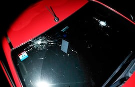 Vehículo rojo con parabrisas fracturado, mostrando daños significativos en el exterior, sin presencia de personas.