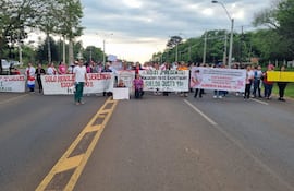 Grupo de manifestantes con pancartas en la carretera, destacando mujeres con camisetas rosas y blancas, expresando sus demandas laborales.