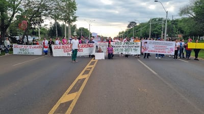 Grupo de manifestantes con pancartas en la carretera, destacando mujeres con camisetas rosas y blancas, expresando sus demandas laborales.