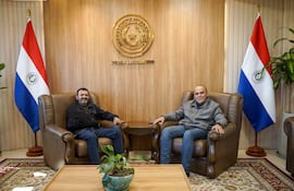 Basilio Núñez sonríe mientras conversa con Miguel Del Puerto en una oficina decorada con banderas paraguayas.