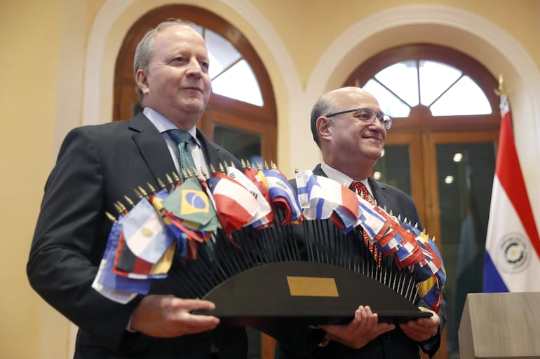 AME2649. ASUNCIÓN (PARAGUAY), 10/03/2026.- El ministro de Economía y Finanzas de Paraguay, Carlos Fernández (i) sostiene banderas junto al presidente del Banco Interamericano de Desarrollo BID, Ilan Goldfajn en una rueda de prensa este martes, en Asunción (Paraguay). El BID inicia sus reuniones anuales en Asunción con la meta de seguir consolidando los esfuerzos de sus tres entidades principales y de analizar grandes retos para Latinoamérica y el Caribe, como la necesidad de crear cadenas de valor para la industria de minerales críticos o la de estimular la competencia regional. EFE/ Juan Pablo Pino
