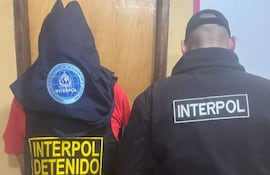 Dos personas visten chaquetas de Interpol; uno lleva capucha y chaleco con la inscripción 'INTERPOL DETENIDO'.