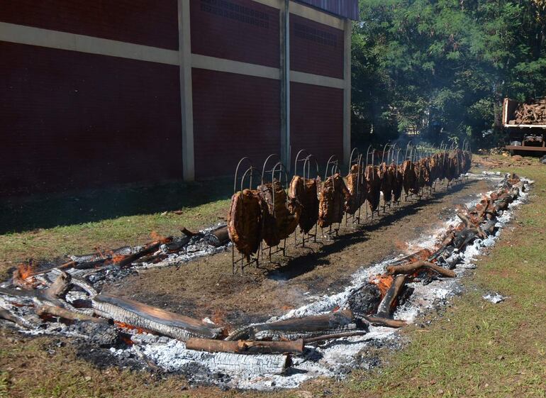 Parrillas con carne cocinándose a la leña en un evento al aire libre rodeado de un ambiente festivo.