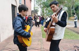 Matías Otazú con chaqueta negra y guitarra amarilla, mientras Víctor González, en suéter negro, toca guitarra marrón para un público atento.