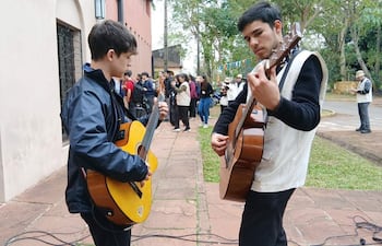 Matías Otazú con chaqueta negra y guitarra amarilla, mientras Víctor González, en suéter negro, toca guitarra marrón para un público atento.