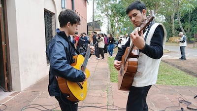 Matías Otazú con chaqueta negra y guitarra amarilla, mientras Víctor González, en suéter negro, toca guitarra marrón para un público atento.