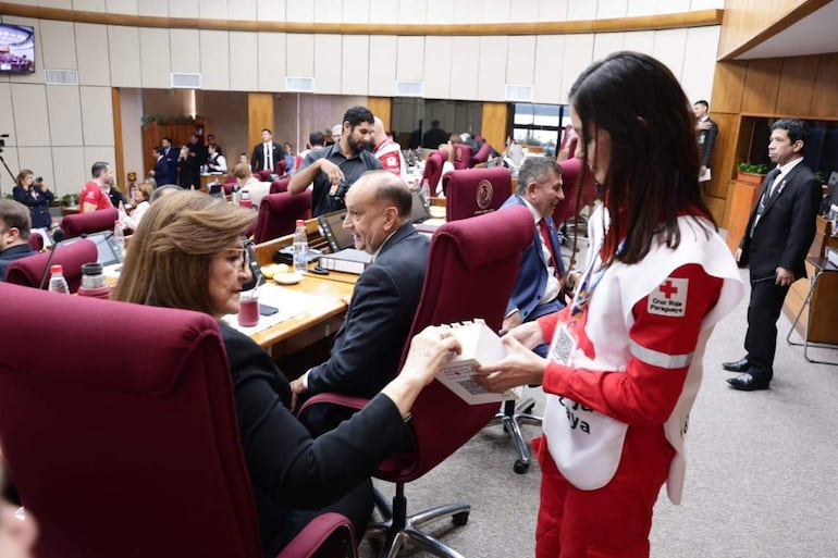 Blanca Margarita Ovelar de Duarte en uniforme de Cruz Roja, junto a Luis Alberto Pettengill, en salón legislativo con asistentes en segundo plano.