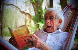 Gregorio Gómez Centurión, hombre mayor con cabello blanco y lentes, sentado en hamaca leyendo un libro en un entorno natural.