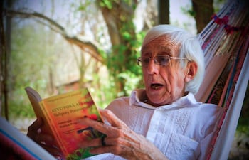 Gregorio Gómez Centurión, hombre mayor con cabello blanco y lentes, sentado en hamaca leyendo un libro en un entorno natural.