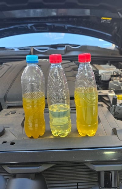 Tres botellas de plástico sobre un motor de automóvil, con líquidos amarillentos, en un entorno exterior despejado.