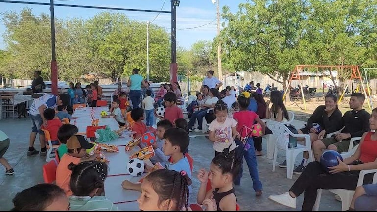 Varios niños sentados alrededor de mesa difrutando de la merienda y obsequios