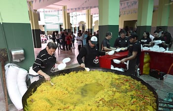 Grupo de personas sirviendo arroz en platos de cartón, con decoración de banderines en ambiente festivo.