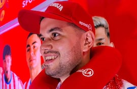 Hombre con camiseta de rayas rojas y blancas y gorra roja que dice 'ROJA', sonríe frente a imágenes de jugadores en un fondo gráfico rojo.