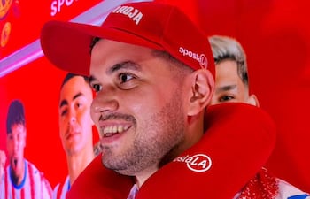 Hombre con camiseta de rayas rojas y blancas y gorra roja que dice 'ROJA', sonríe frente a imágenes de jugadores en un fondo gráfico rojo.