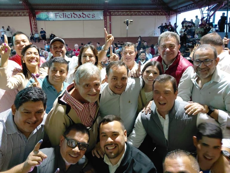 Grupo de personas sonrientes en celebración, con ropa casual y brazos levantados en un ambiente festivo decorado con un cartel que dice 'Felicidades'.