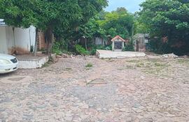 Espacio exterior con superficie de piedra, construcción pequeña con techo naranja rodeada de vegetación en abandono.